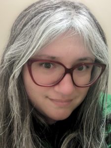 A woman with gray bangs, dark hair, and red glasses.